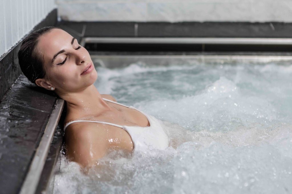 Side view of beautiful woman lying with closed eyes and enjoying hot bubbling bath during spa session